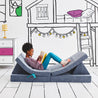 Girl journaling and lying on the Reclined Reader configuration of the Yourigami Kids Play Couch in blue-lagoon color with a gaming console in stash pocket 