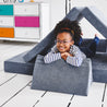 Girl lying on her stomach inside a tunnel configuration of the Yourigami Kids Play Couch in blue-lagoon color with her arms and feet resting on the triangle pieces