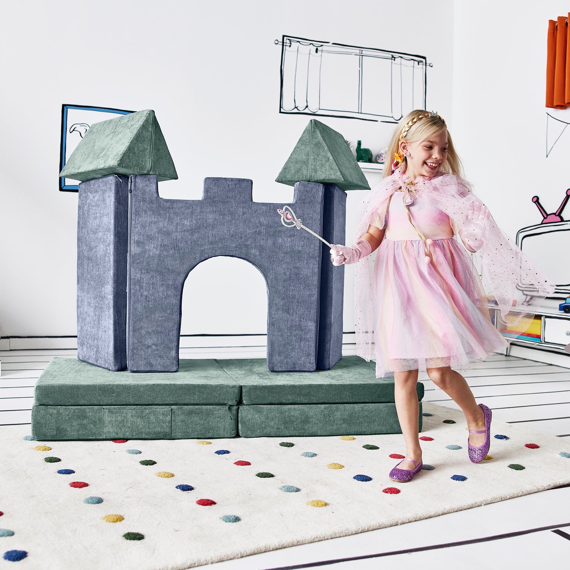 Girl dressed as a princess running past the deluxe castle configuration of the Yourigami Kids Play Castle in blue-lagoon color and the Yourigami Kids Play Couch in green-meadows color