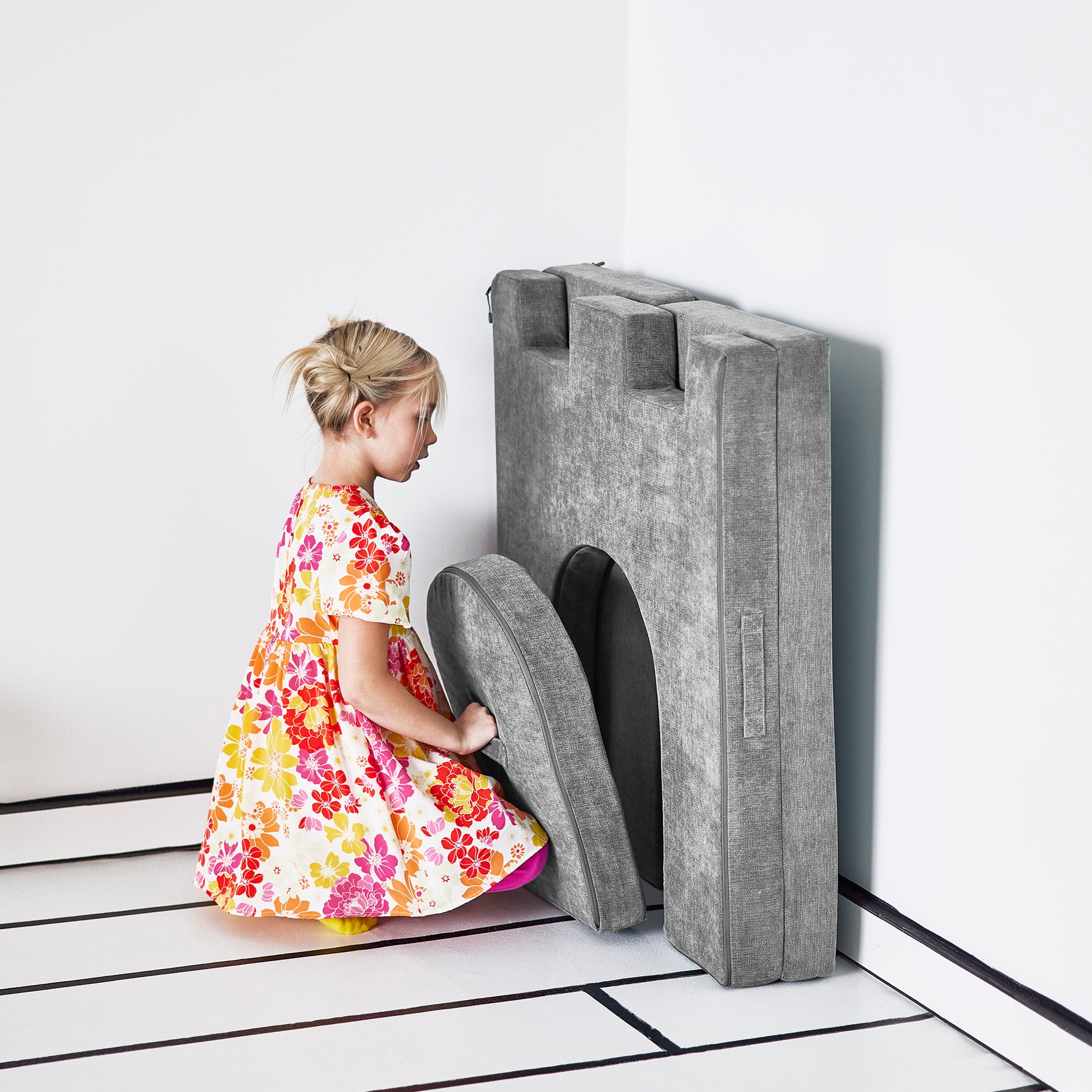 Girl places the drawbridge piece of the Yourigami Kids Play Castle in mountain-gray color to fit neatly in the folded doorway piece against the wall