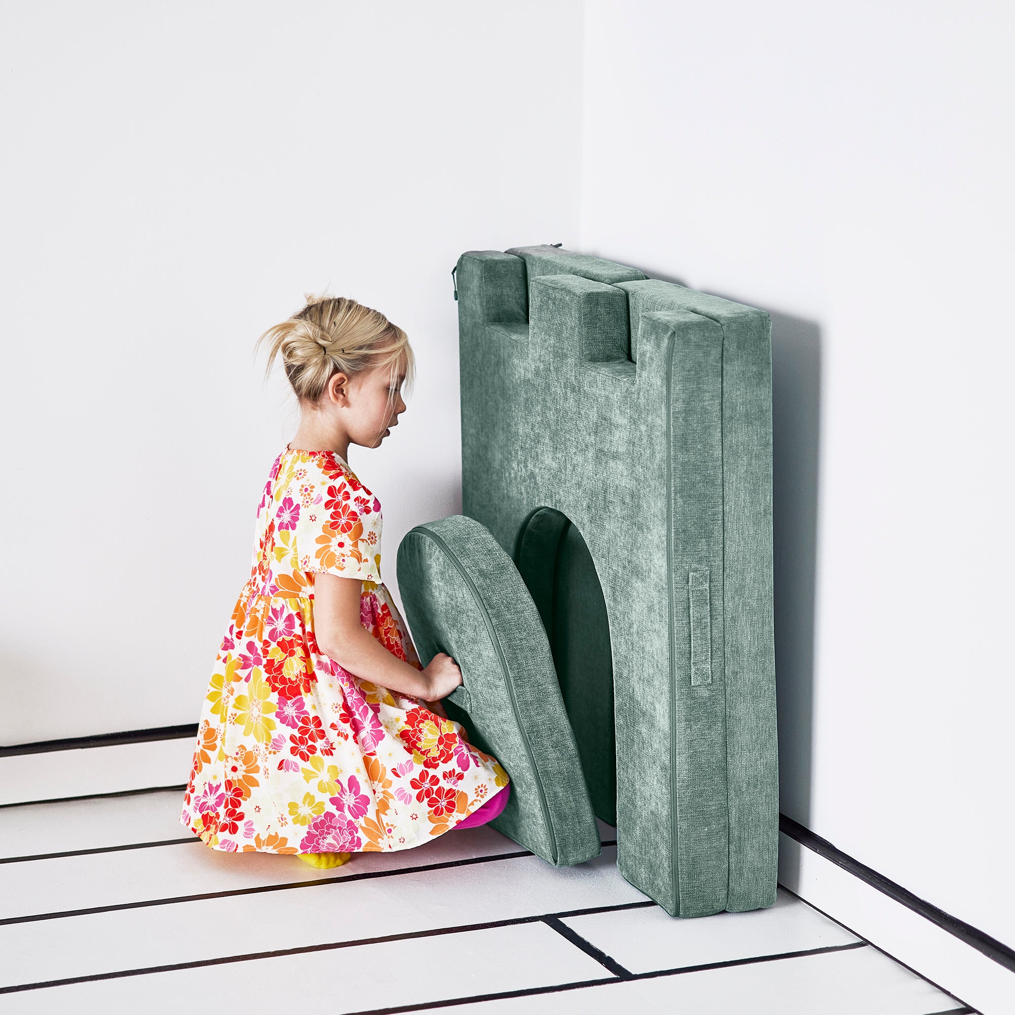 Girl places the drawbridge piece of the Yourigami Kids Play Castle in green-meadows color to fit neatly in the folded doorway piece against the wall
