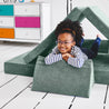 Girl lying on her stomach inside a tunnel configuration of the Yourigami Kids Play Couch in green-meadows color with her arms and feet resting on the triangle pieces