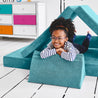 Girl lying on her stomach inside a tunnel configuration of the Yourigami Kids Play Couch in tropical-teal color with her arms and feet resting on the triangle pieces