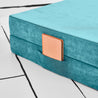 Close-up view of the base hinged panel piece of the Yourigami Kids Play Couch in tropical-teal color with a journal tucked into the stash pocket of the cover