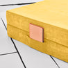Close-up view of the base hinged panel piece of the Yourigami Kids Play Couch in sunflower-yellow color with a journal tucked into the stash pocket of the cover