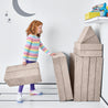 Girl folding and stacking the pieces of the Yourigami Kids Play Fort in beige-sands against the corner of the playroom for storage