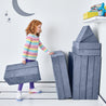 Girl folding and stacking the pieces of the Yourigami Kids Play Fort in blue-lagoon against the corner of the playroom for storage