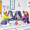 Children pretending to roast marshmallows at a play fire and resting on the Cozy Campsite configuration of the Yourigami Kids Play Fort in cosmic-purple color