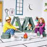 Children pretending to roast marshmallows at a play fire and resting on the Cozy Campsite configuration of the Yourigami Kids Play Fort in green-meadows color