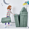 Girl folding and stacking the pieces of the Yourigami Kids Play Fort in green-meadows against the corner of the playroom for storage