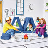 Children pretending to roast marshmallows at a play fire and resting on the Cozy Campsite configuration of the Yourigami Kids Play Fort in sapphire-caves color